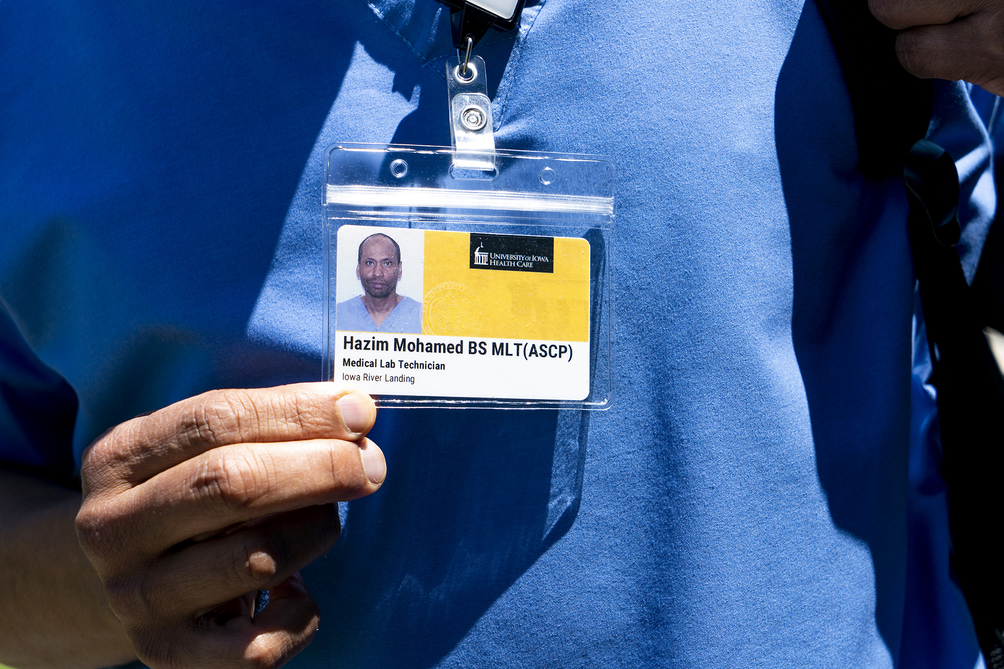 Mohamed holds his University of Iowa Hospitals and Clinics badge in front of his blue scrubs.