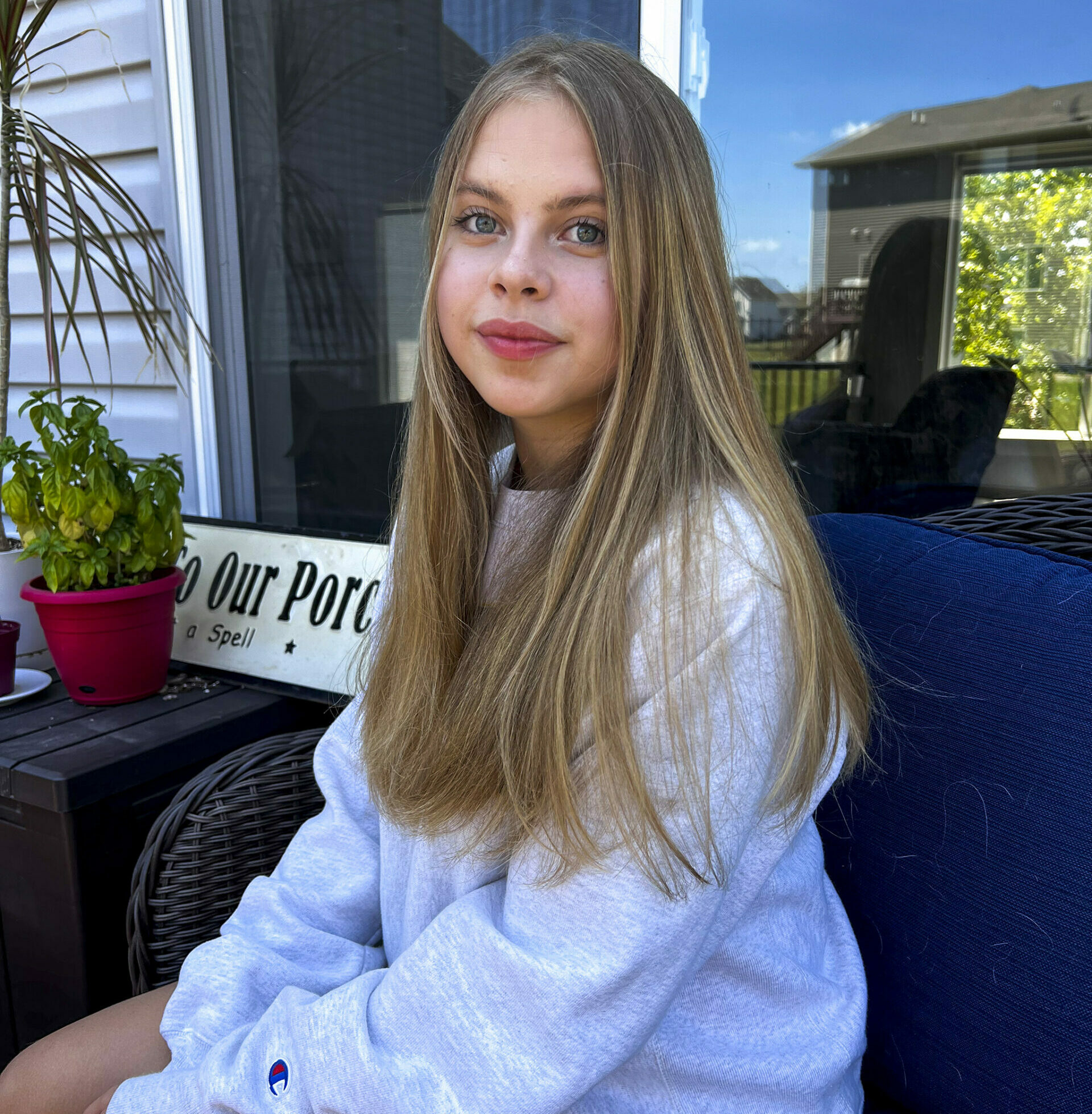 Liza sits on porch furniture in her backyard. She looks at the camera with a slight smile and wears a gray sweatshirt.