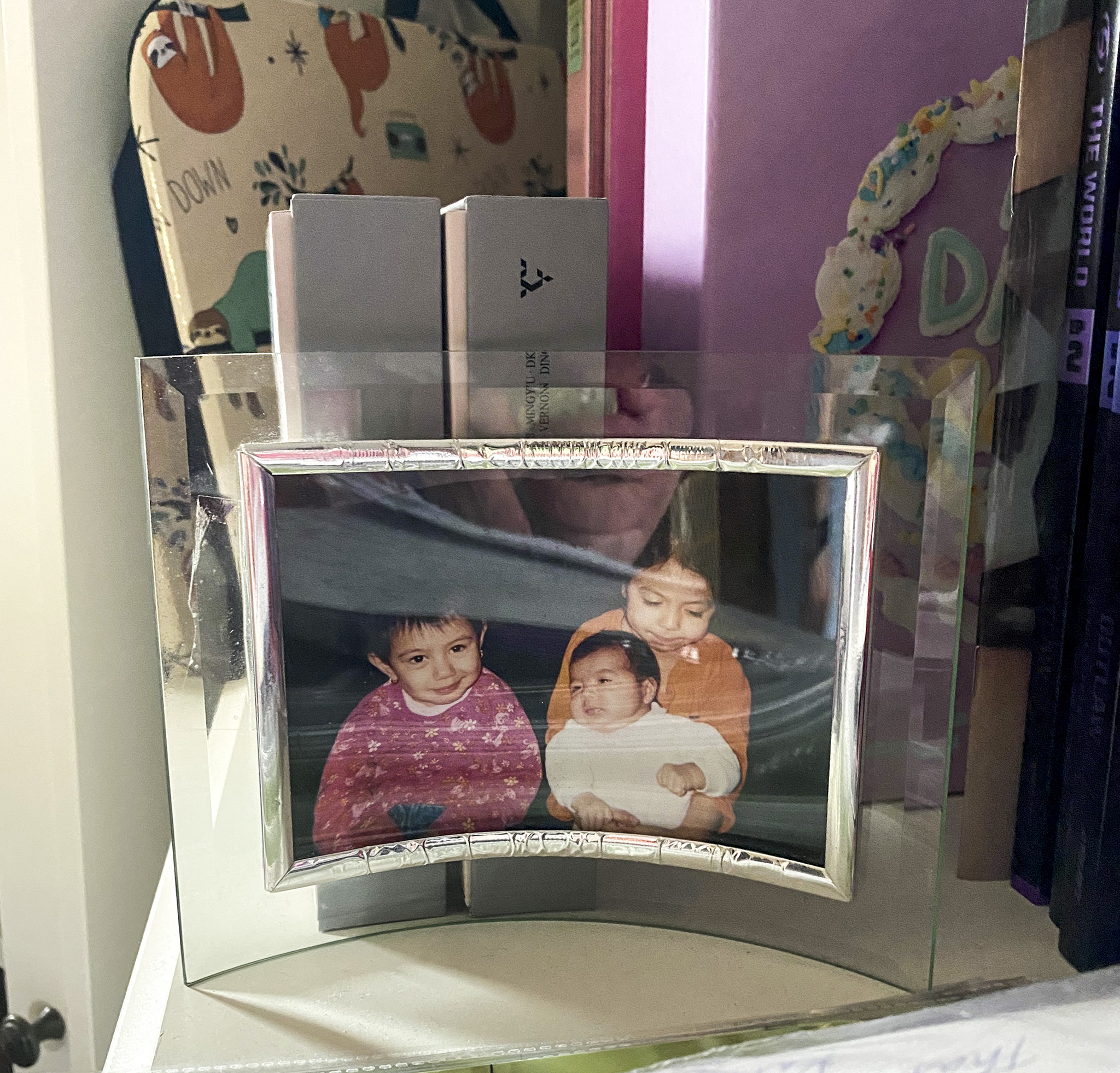 A glass framed photo of three little girls sits on a white dresser. The photo is of Iran Carlos-Martinez and her two younger sisters.